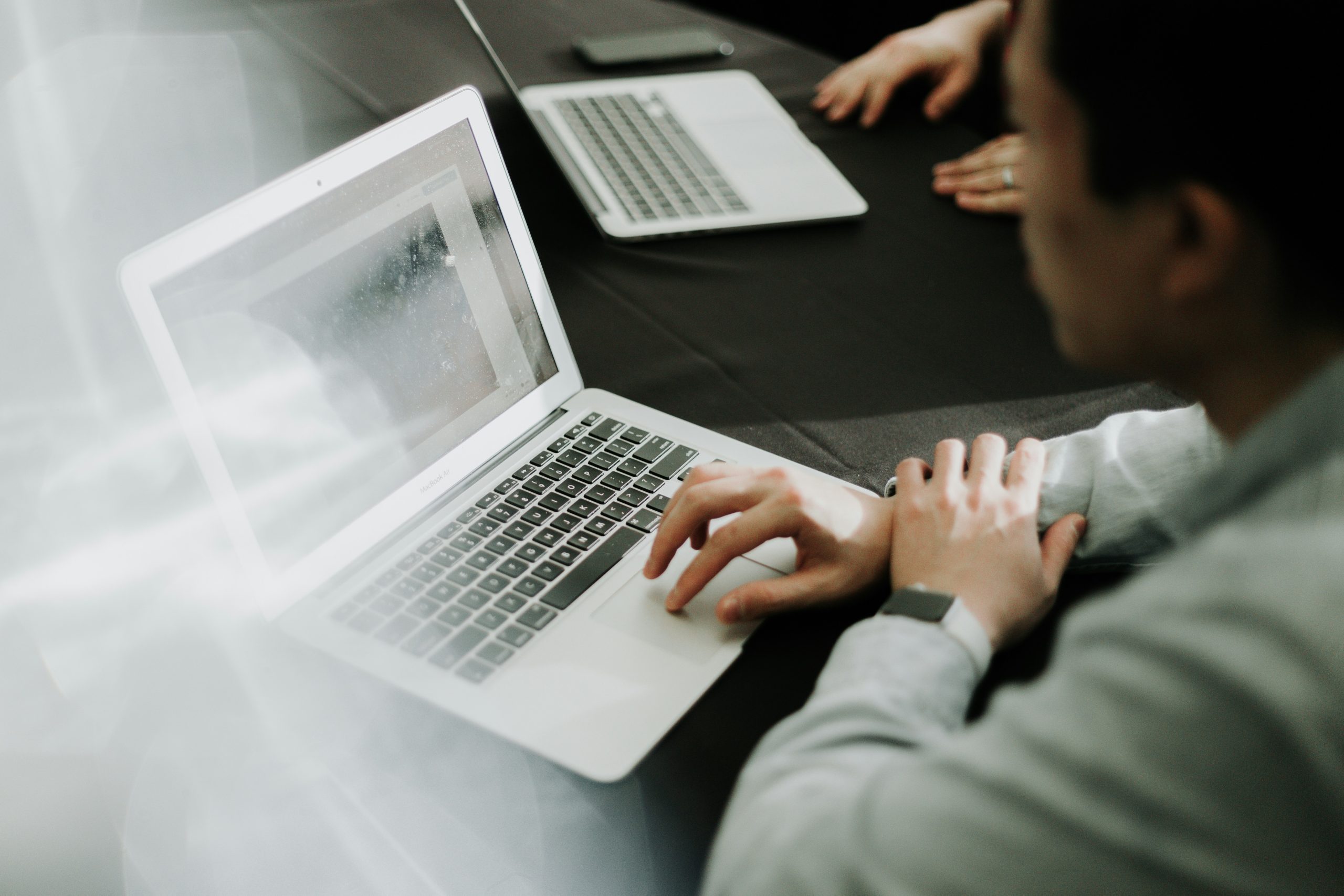 alt="A couple of people use their laptops while sitting at a table with a black tablecloth."